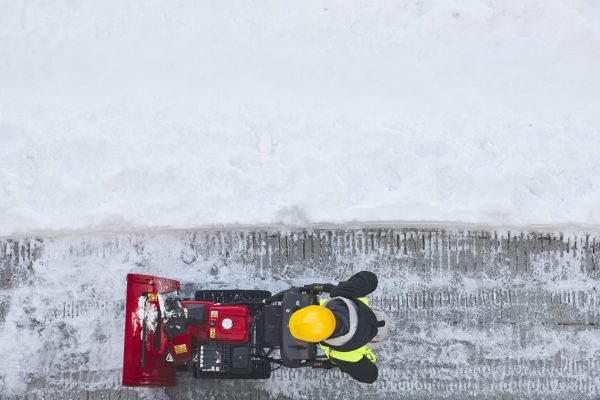 Worker cleaning snow on the sidewalk with a snowblower. Maintenance